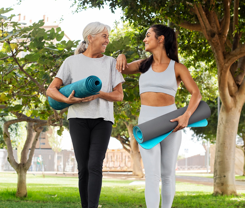 Two women holding yoga mats outdoors in a park setting